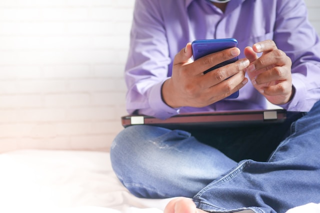 Man with a laptop on his lap while sitting on a bed and playing online slots